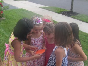 The girls huddle around and READ a clue to find Amber the Orange Fairy.